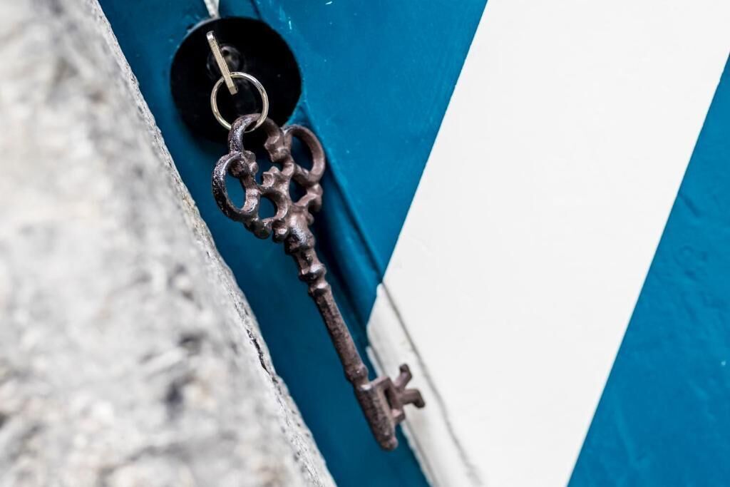 Primer plano de una llave vieja y oxidada colgada en una puerta azul y blanca.