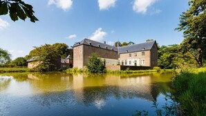 Un edifici gran i antic amb un estany al davant, envoltat de vegetació exuberant.