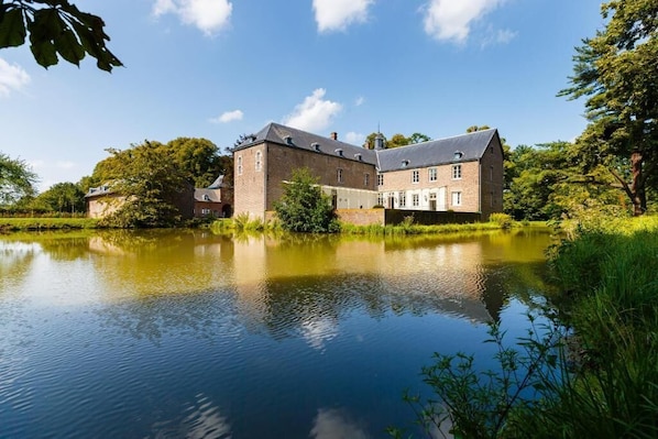 A large, historic building with a pond in front, surrounded by lush greenery. - Kasteel Wolfrath (Born)