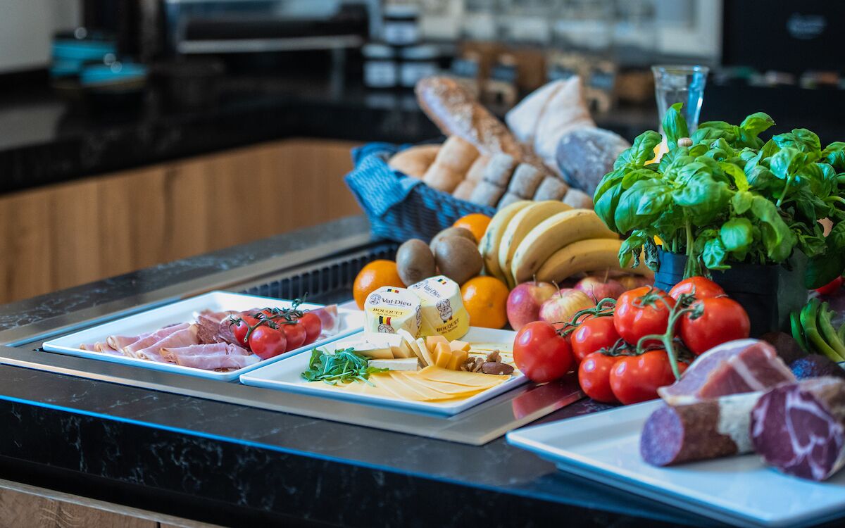 A kitchen counter with various food items including meats, cheeses, tomatoes, and a basil plant.