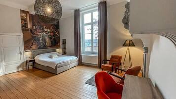 A modern hotel room with a large bed, a red armchair, a floor lamp, and a painting on the wall.