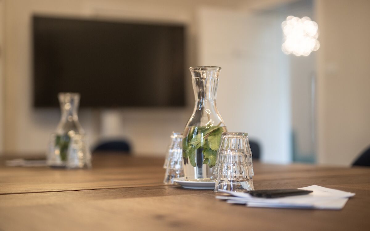 Een houten tafel met glazen vaasjes en een enkel bord, een zwart object en een witte servet.