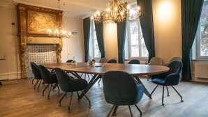 Una sala de conferències amb una taula rodona, sis cadires, una làmpada penjant, una llar de foc i grans finestres amb cortines.
