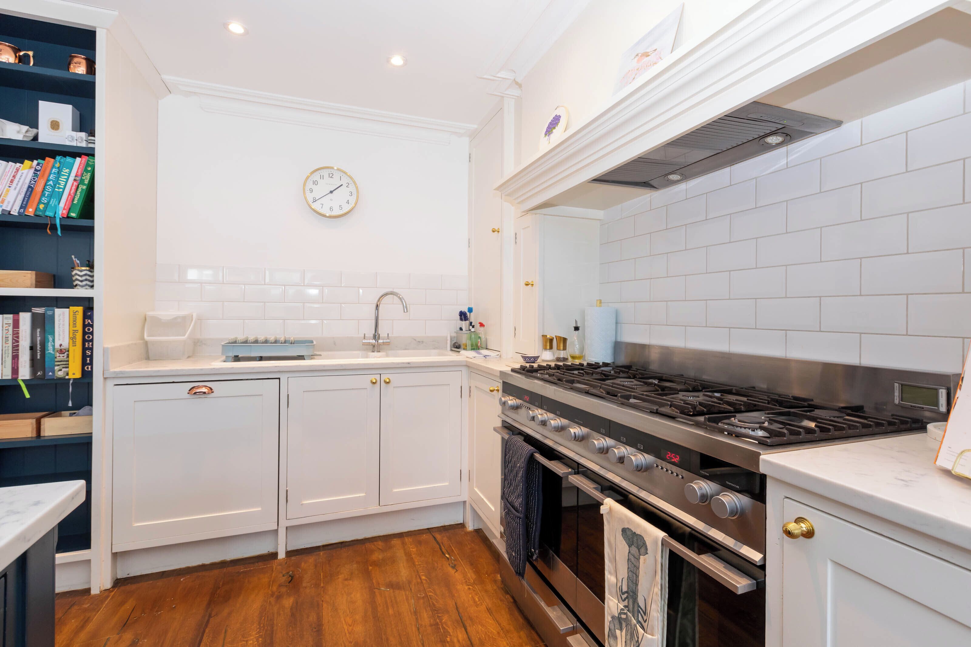 A modern kitchen with white cabinetry, a stainless steel stove, and a clock on the wall.
