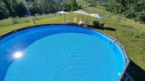 Una piscina azul cristalina rodeada de césped con sillones reclinables y sombrillas.
