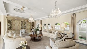 A spacious living room with a high ceiling, elegant chandeliers, and a large window offering a view of greenery. - Wild Cane Ridge 2 by Island Villas (Westmoreland)
