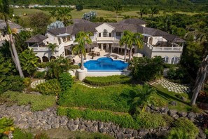 A large house with a swimming pool, surrounded by tropical vegetation and palm trees. - Wild Cane Ridge 2 by Island Villas (Westmoreland)