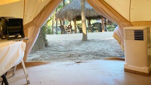 Una carpa con una mesa y un equipo de aire acondicionado en su interior, y una estructura de techo de paja en el exterior.