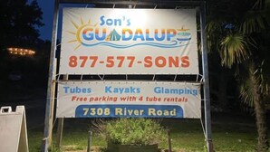 Señal de Son's GundaLup ofreciendo tubos, kayaks y glamping, con estacionamiento gratuito y 4 alquileres de tubos.