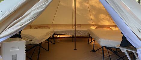 A tent with two beds, a white refrigerator, and a portable heater.