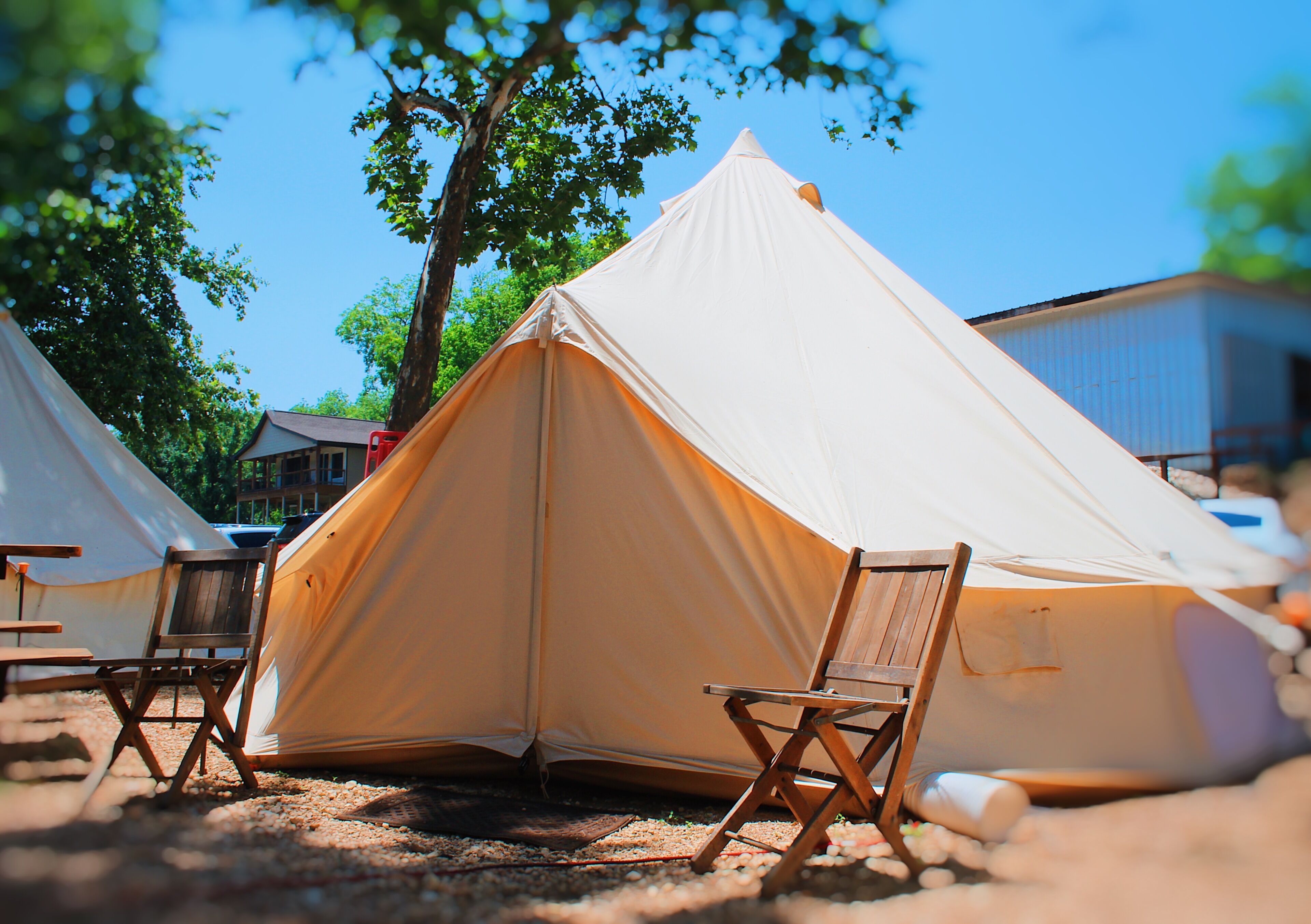 Une rangée de tentes, devant lesquelles sont disposées des chaises pliantes, est installée dans un espace ouvert, avec des arbres et des bâtiments en arrière-plan.