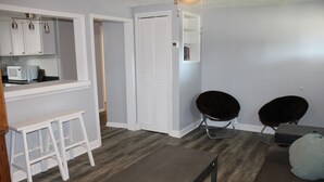 Een moderne keuken met witte kastjes, een magnetron en een witte kruk. Er is een donker houten bankje en twee zwarte stoelen.
