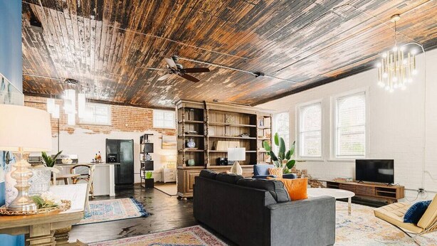 Un salon spacieux avec un canapé noir, des étagères en bois, un téléviseur et une grande fenêtre.