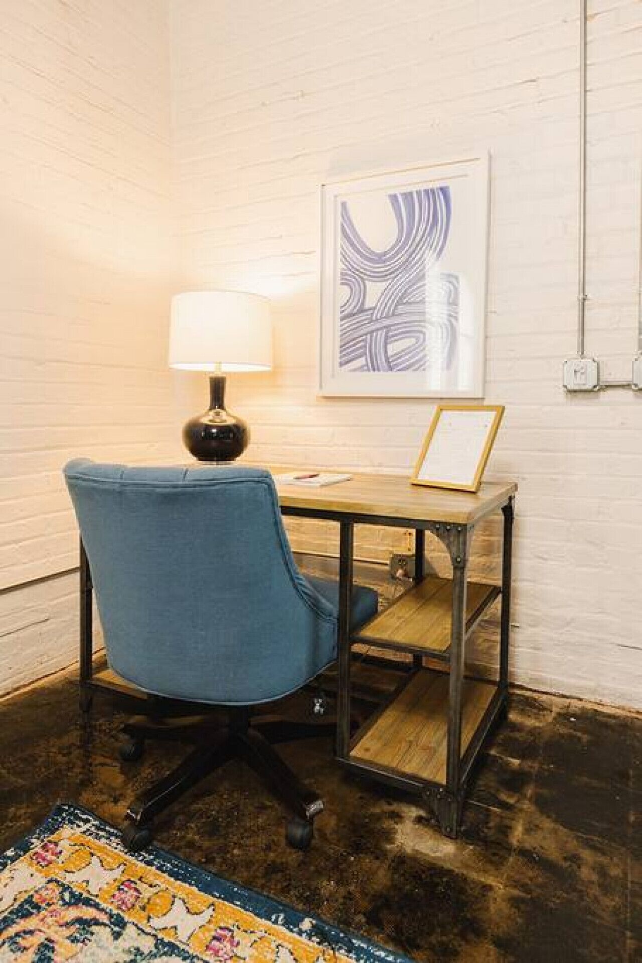 A room with a blue chair, a small wooden table, a framed picture, and a lamp.