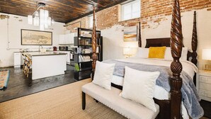 Une chambre spacieuse avec un lit à baldaquin, un coin salon avec un banc, un coin cuisine et un coin repas.