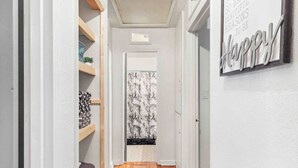A narrow hallway with wooden flooring, white walls, and a ceiling with a recessed light. There is a door at the end of the hallway, and a wall with a 'Happy' sign. - Gator Getaway ~ close to UF & hospitals (Gainesville)