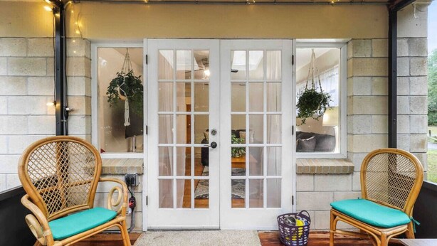 A cozy entrance with a white door, two wicker chairs with teal cushions, and hanging plants. - Gator Getaway ~ close to UF & hospitals (Gainesville)