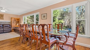A dining area with a wooden table and chairs, a sofa, and a bookshelf.