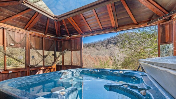 A hot tub under a wooden roof with a view of a forested hillside.