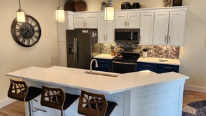 A modern kitchen with white cabinetry, a central island with bar stools, a stainless steel refrigerator, a microwave, and a kettle on the stove. - LUXURY WINDSOR HILLS 4 BR 5BA POOL & SPA HOME 2.5 MILES to DSNY +++ (Kissimmee)