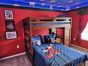Ein Etagenbett mit blauer und roter Bettwäsche, einer von Sternen verzierten Decke und gerahmten Bildern von Disney und einem Schloss an der Wand.