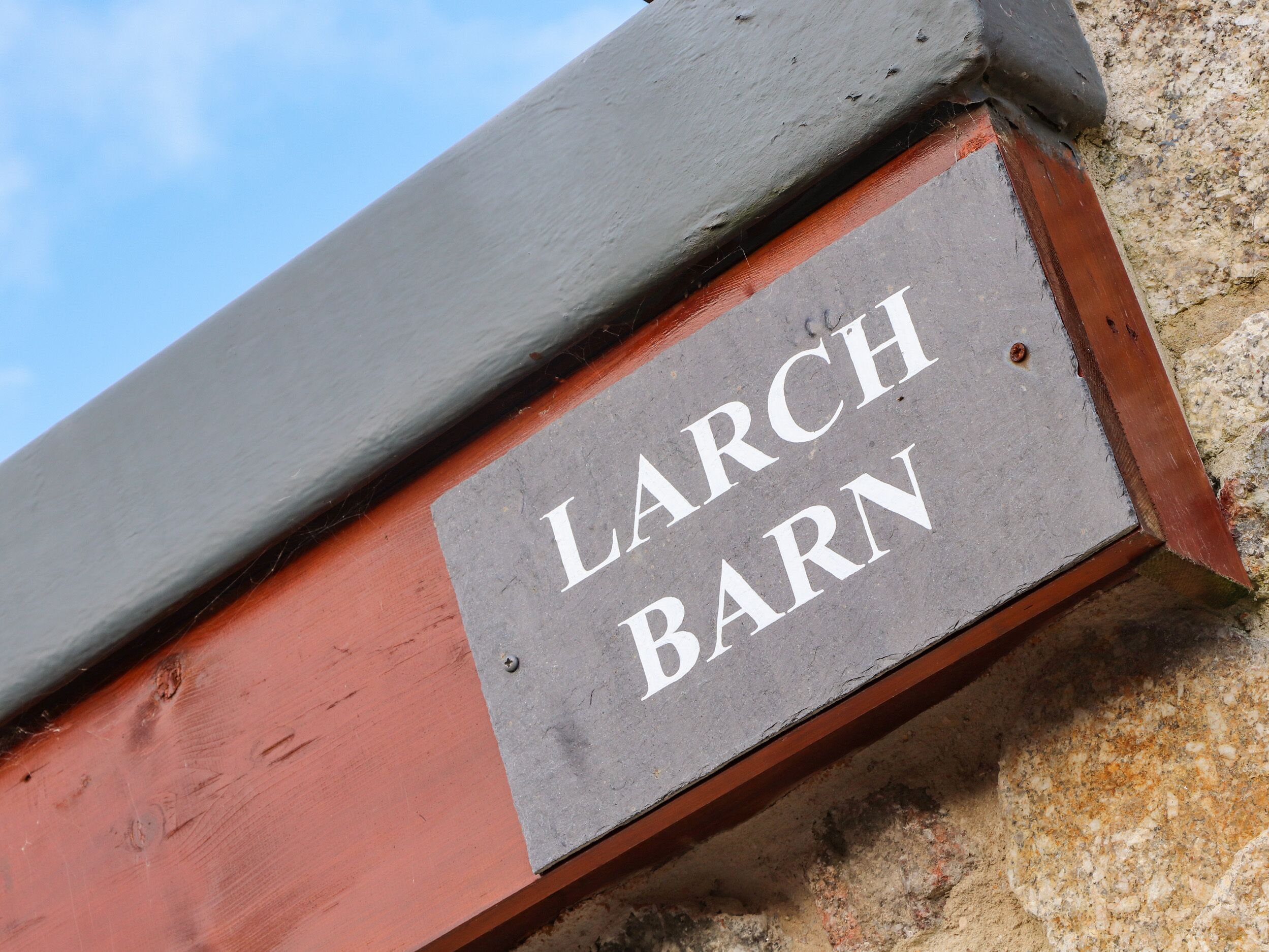 A sign with the text "LARCH BARN" on a grey background attached to a red and grey structure.