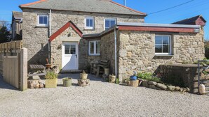 A stone house with a red roof, a front door, and a small porch area with potted plants. - Larch Barn (Helston)