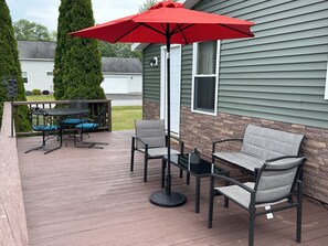 Une terrasse dotée de mobilier d’extérieur, comprenant des chaises et une table, ainsi qu’un parasol rouge.