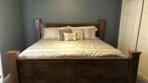 A wooden bed with a patterned bedspread and pillows in a room with a gray wall and a white door.