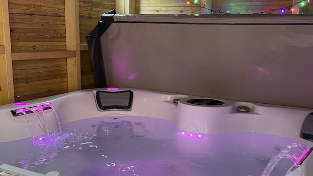 A hot tub with a control panel and a digital display, surrounded by wooden walls and string lights.