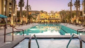 Área de piscina de hotel com hidromassagem, espreguiçadeiras e palmeiras.