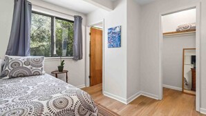 A bedroom with a bed, a window, a door, and a small table with a plant. - The Hoggtown Hideaway (Gainesville)