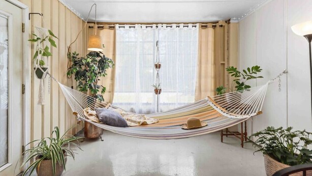 A hammock in a room with a large window, a hanging lamp, and several potted plants. - The Hoggtown Hideaway (Gainesville)