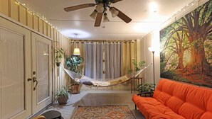 A living room with a hammock, orange sofa, patterned rug, and a large forest-themed painting. - The Hoggtown Hideaway (Gainesville)