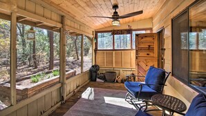 A wooden cabin with a covered porch, a ceiling fan, a large window, and a chair. - Deck & Grill: Pet-Friendly Lakeside Cabin (Lakeside)