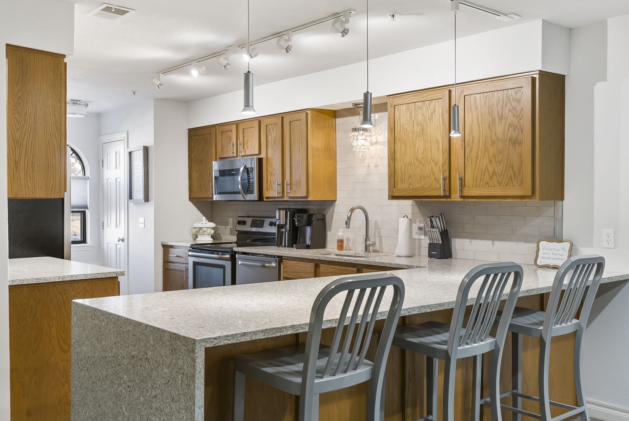 A modern kitchen with wooden cabinets, granite countertops, stainless steel appliances, and bar stools.