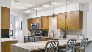 A modern kitchen with wooden cabinets, granite countertops, stainless steel appliances, and bar stools. - 2 bedroom, 2 bath ground floor condo with indoor pool minutes from Branson strip (Branson)