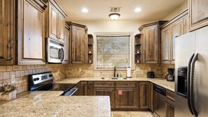 A kitchen with granite countertops, wooden cabinets, a stainless steel refrigerator, and a built-in microwave.