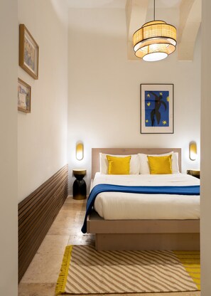 A hotel room with a bed, bedside lamps, a framed artwork, and a hanging light fixture.