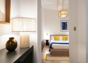 Quarto de hotel moderno com cama, luminárias de cabeceira, um vaso e um quadro na parede.