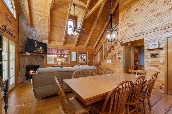 Cozy cabin interior with a central seating area, stone fireplace, and staircase to an upper level.