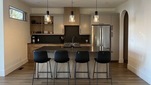 Une cuisine moderne dotée d’un îlot central, d’appareils électroménagers en acier inoxydable et de luminaires suspendus.
