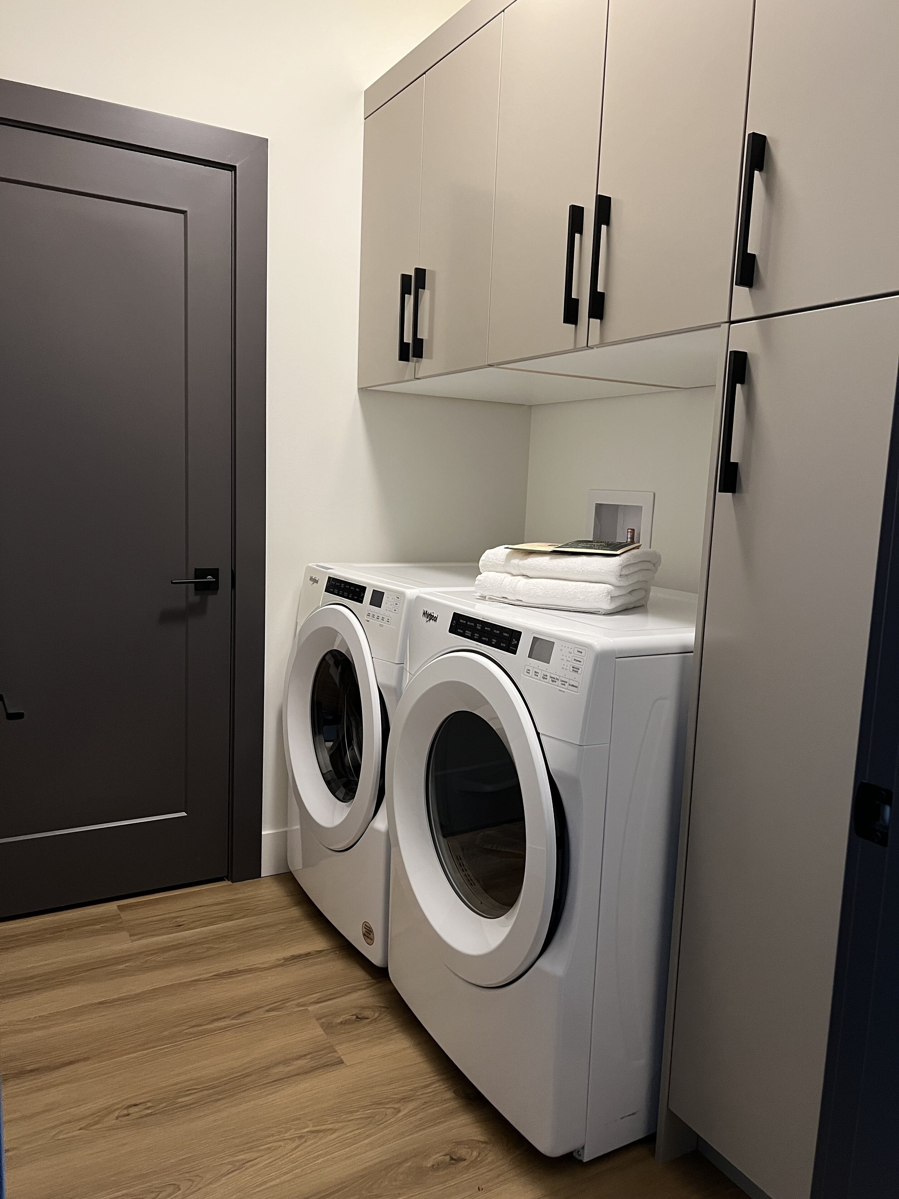 A laundry room with two front-loading washing machines, a dryer, and a door.