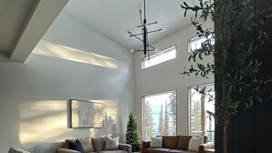 Un salon spacieux avec un plafond haut, une grande fenêtre, un lustre moderne et une plante en pot.