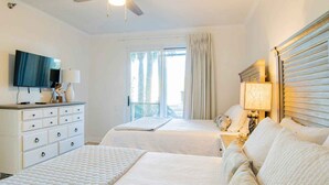 A hotel room with two beds, a ceiling fan, a TV, a dresser, and a window with curtains. - Beach Colony West #1D | Large Patio & Many Community Amenities (Perdido Key)