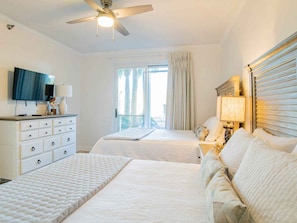 Une chambre d’hôtel avec deux lits, un ventilateur de plafond, une télévision, une commode et une fenêtre avec des rideaux.