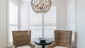 A corner room with two wicker chairs and a table, a chandelier, and white shutters. - Beach Colony West #1D | Large Patio & Many Community Amenities (Perdido Key)