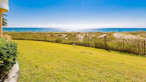 A beachfront property with a grassy lawn, a wooden fence, and a clear view of the ocean. - Beach Colony West #1D | Large Patio & Many Community Amenities (Perdido Key)
