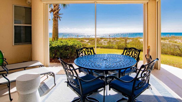 A covered patio with a round table and chairs, overlooking a beach. - Beach Colony West #1D | Large Patio & Many Community Amenities (Perdido Key)