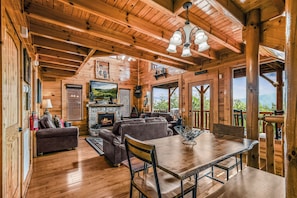 Cozy cabin with a fireplace, comfortable seating, and dining table, offering views of the surrounding landscape.